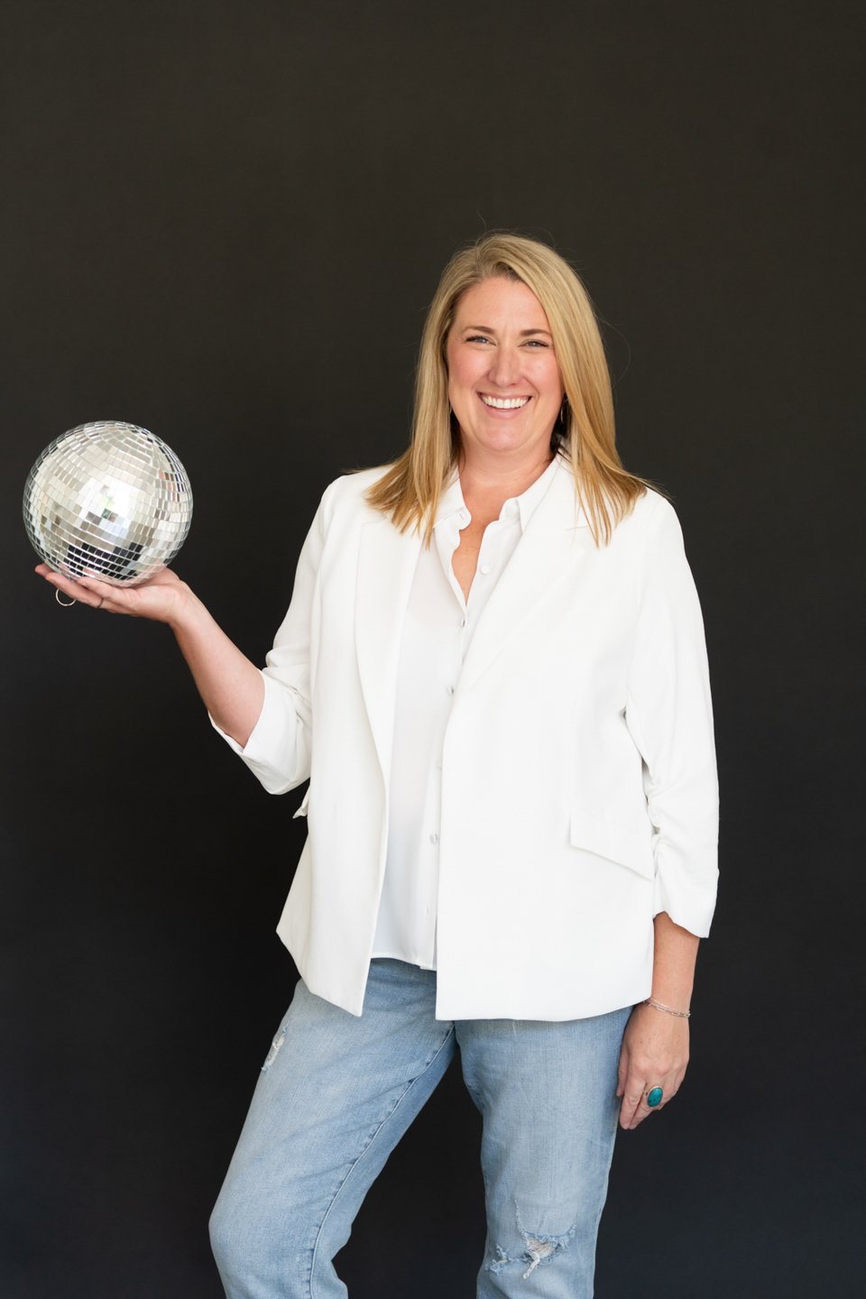 Denver area real estate agent Kathryn Tighe holding a disco ball and smiling, representing winning in a competitive housing market in Arvada and Westminster.