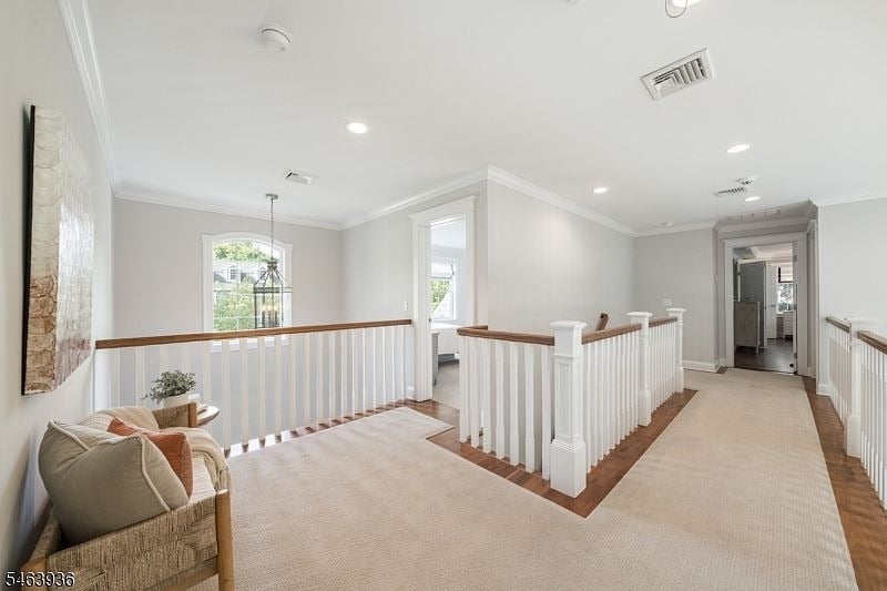 Upstairs landing with white railings, light carpet, and a woven chair by an arched window.