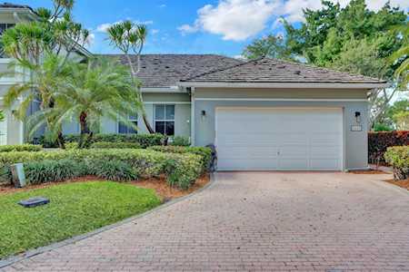 Single-story home with a two-car garage, brick-paver driveway, and tropical landscaping.