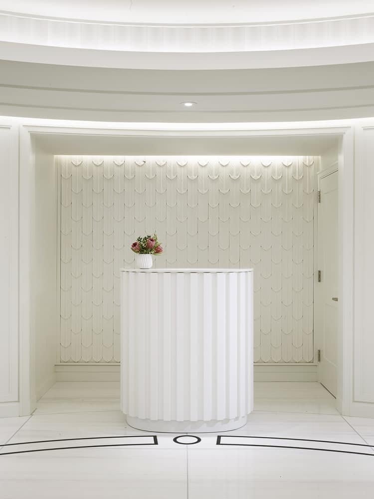 White residential lobby with a curved reception desk and flowers against a scalloped wall.
