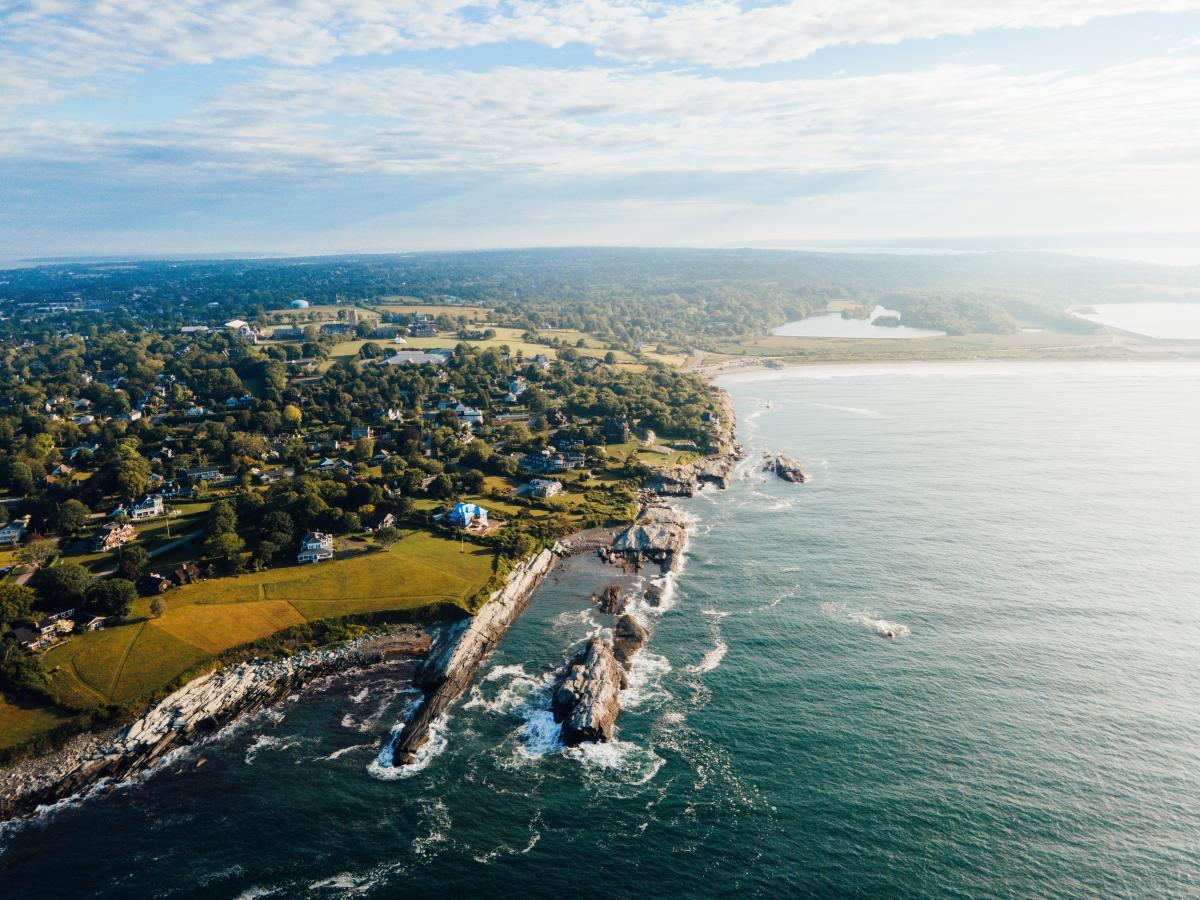 Aerial view of coastal homes and autumn trees along a rocky shoreline.