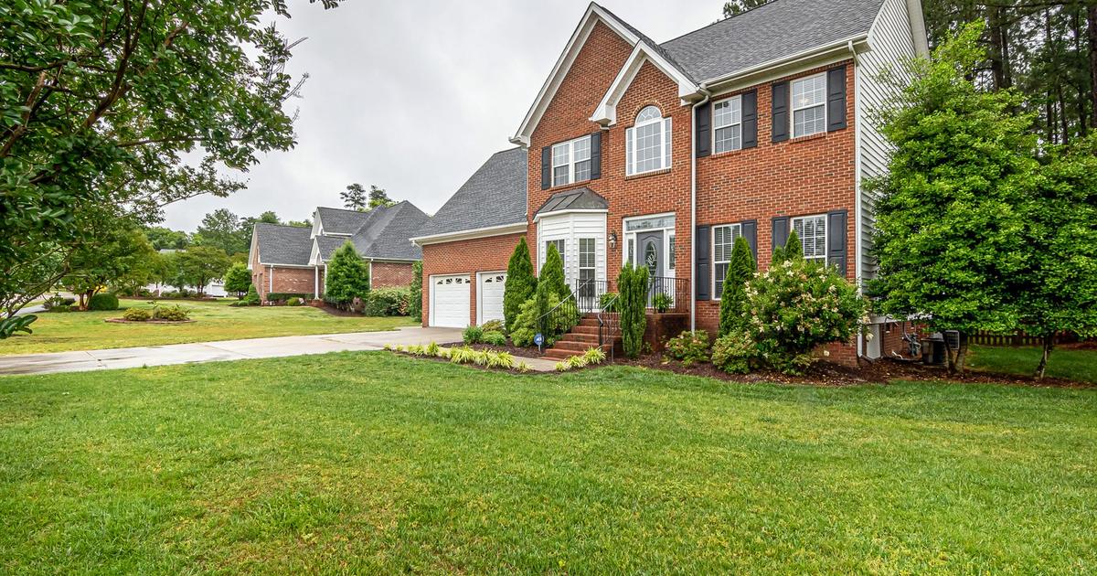 Two-story red brick house with a gabled roof, attached garage, and landscaped front yard on a quiet residential street.