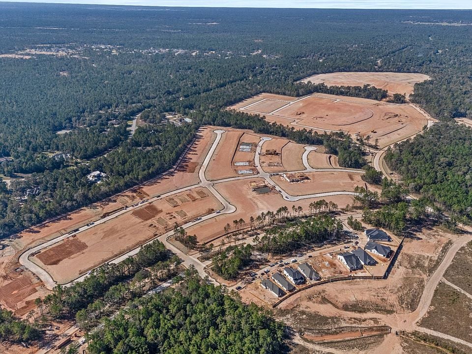 Aerial view of a developing subdivision with curving roads, cleared lots, and wooded surroundings.