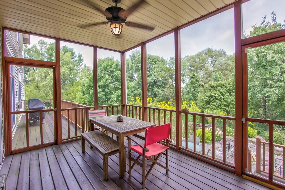 Screened porch with a wooden dining set, ceiling fan, and leafy garden views.