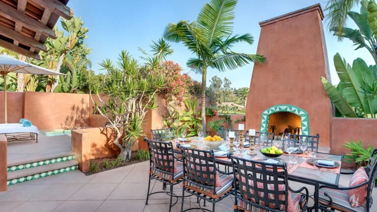 Outdoor dining patio with a terracotta fireplace, tiled steps, and palm trees.