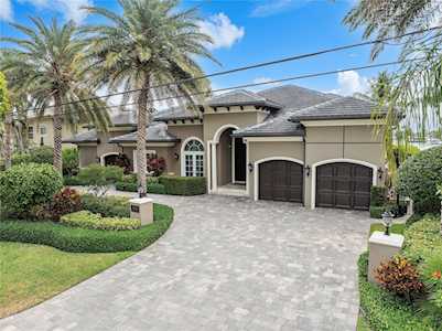 Stucco home with arched entry, double garage, paved driveway, and palm-lined landscaping.