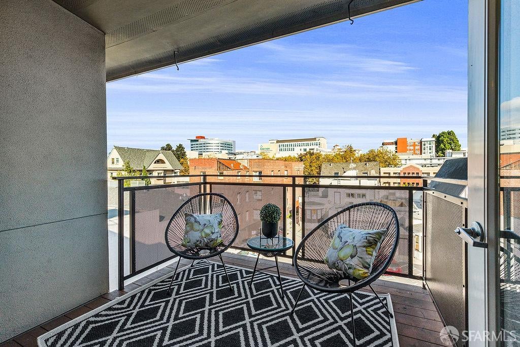 Furnished balcony with woven chairs and a geometric rug overlooking Oakland buildings.