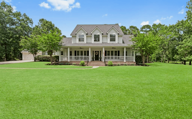White two-story house with three dormers, a covered porch, and a broad green lawn.