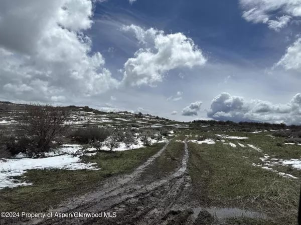 Muddy tracks cross a patchy snow-covered field beneath large clouds.