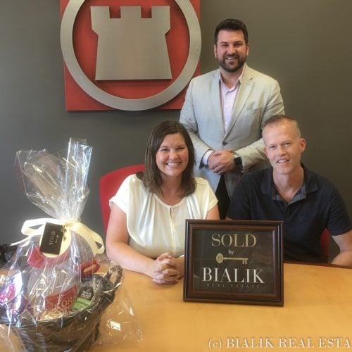 Three adults celebrate a home closing behind a SOLD by Bialik Real Estate plaque.