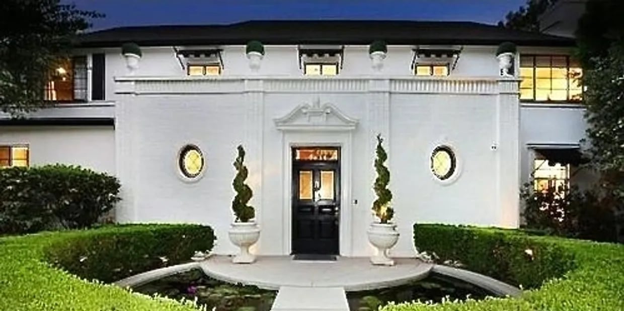 White symmetrical home with a black central entrance, round windows, sculpted topiary, and reflecting pools.