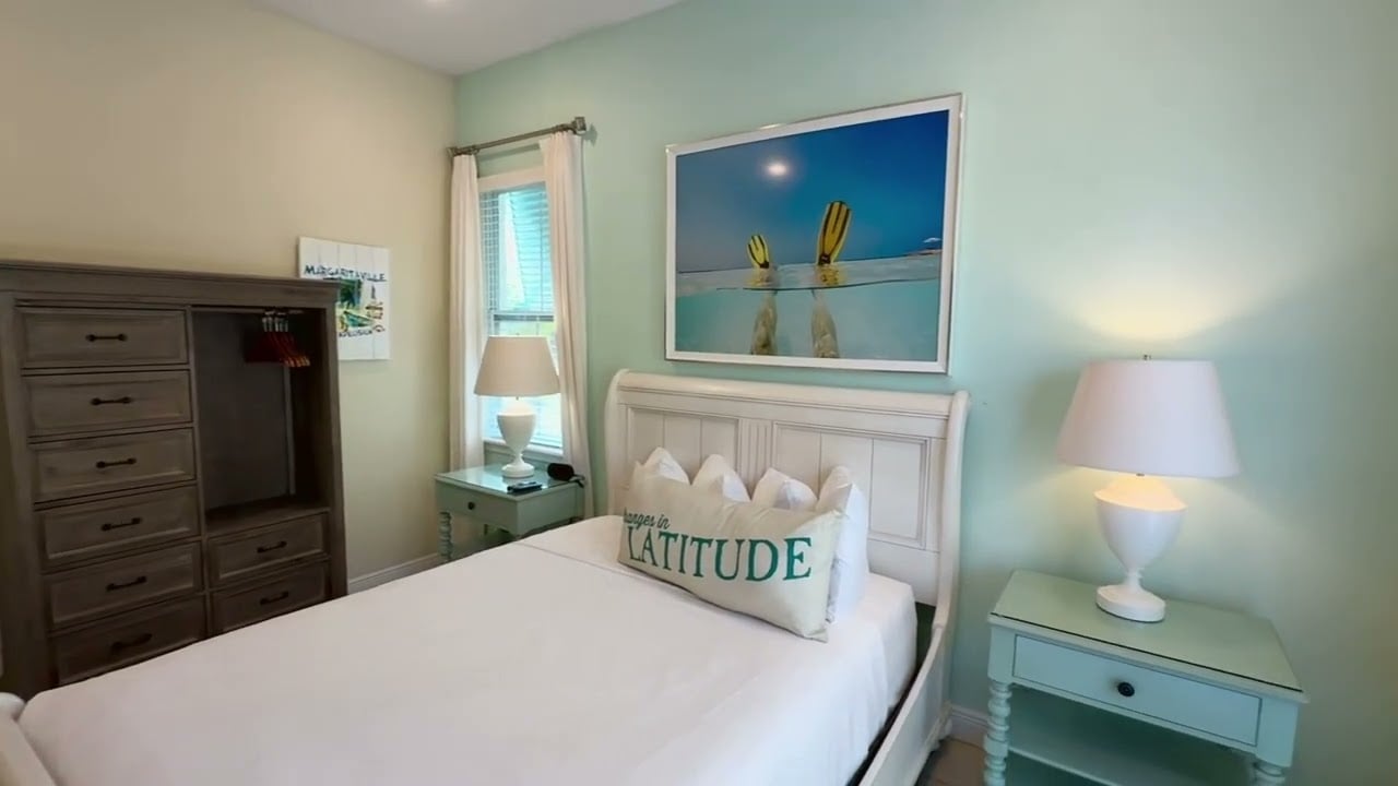 Furnished bedroom with a white bed, aqua walls, and beach-themed artwork above the headboard.