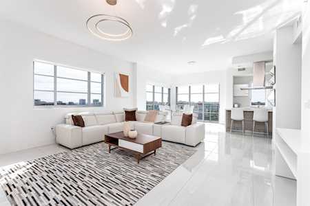 Bright open-plan living room with a white sectional, patterned rug, and kitchen breakfast bar.