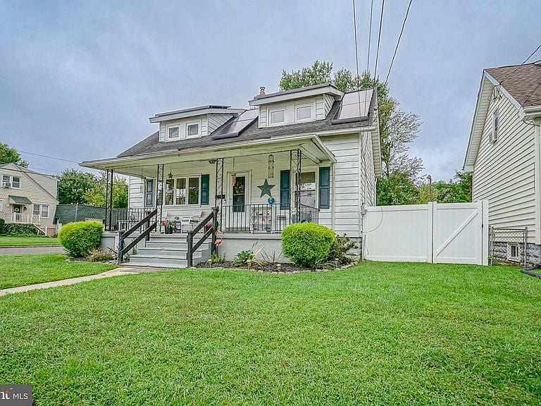 White-sided home with a covered porch, dormers, and a broad front lawn.