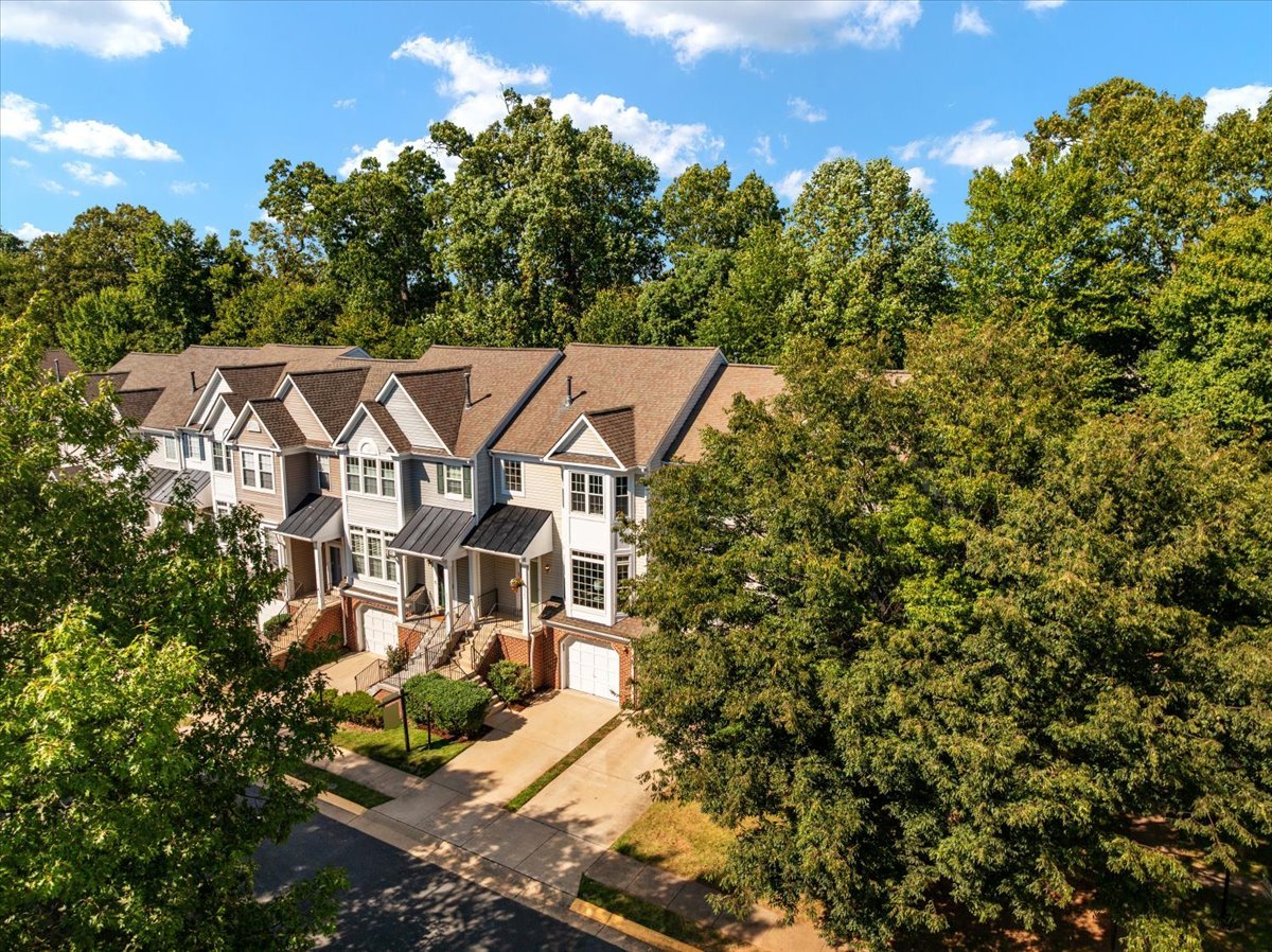 Aerial view of attached townhouses with front-facing garages, driveways, and mature trees.