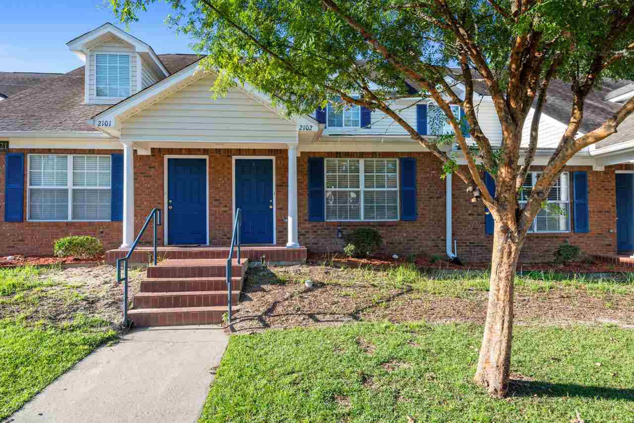 A brick home featuring blue shutters, with a tree standing prominently in front of the house.