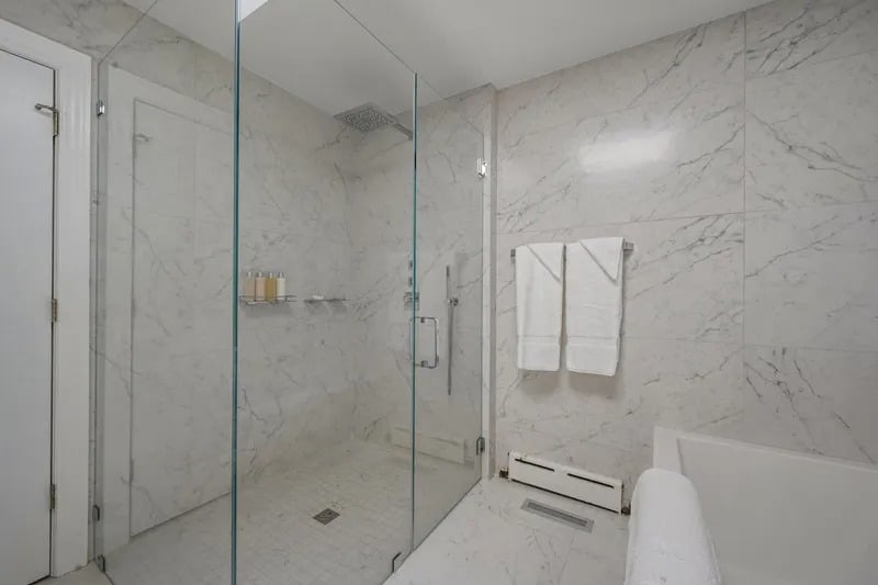 Marble bathroom with a glass-enclosed shower, soaking tub, and white towels.