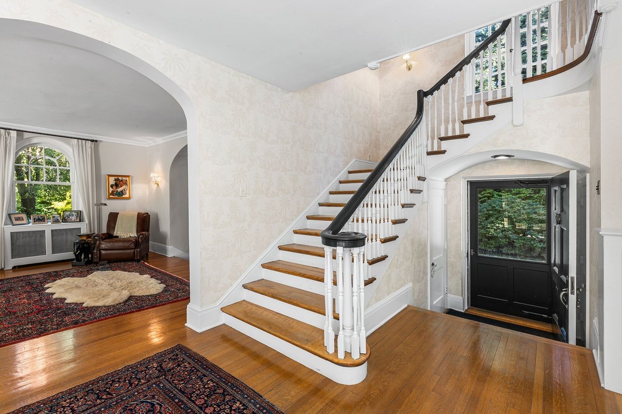 Entry hall with a sweeping staircase, hardwood floors, patterned rugs, and a black glass-panel front door.