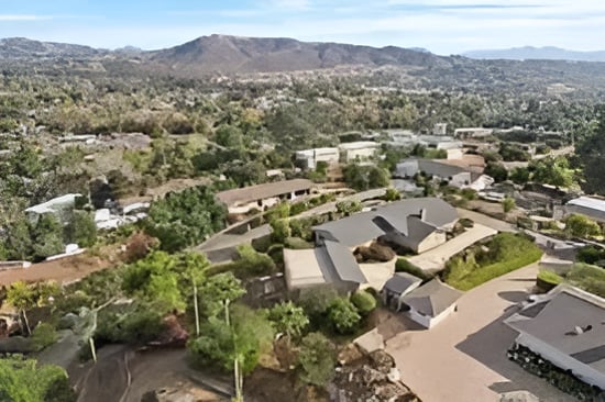 Aerial view of homes and tree-lined streets with mountains in the distance.