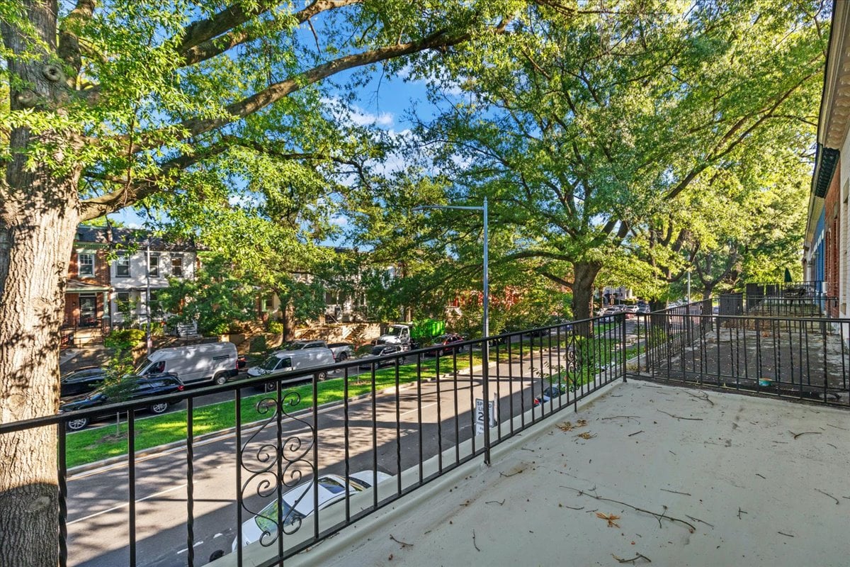 Raised terrace with wrought-iron railing overlooking a leafy, tree-lined residential street.