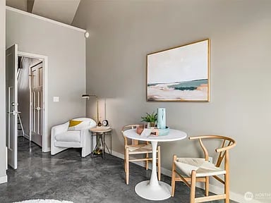 Staged living and dining area with a white sofa, round table, and framed coastal artwork.