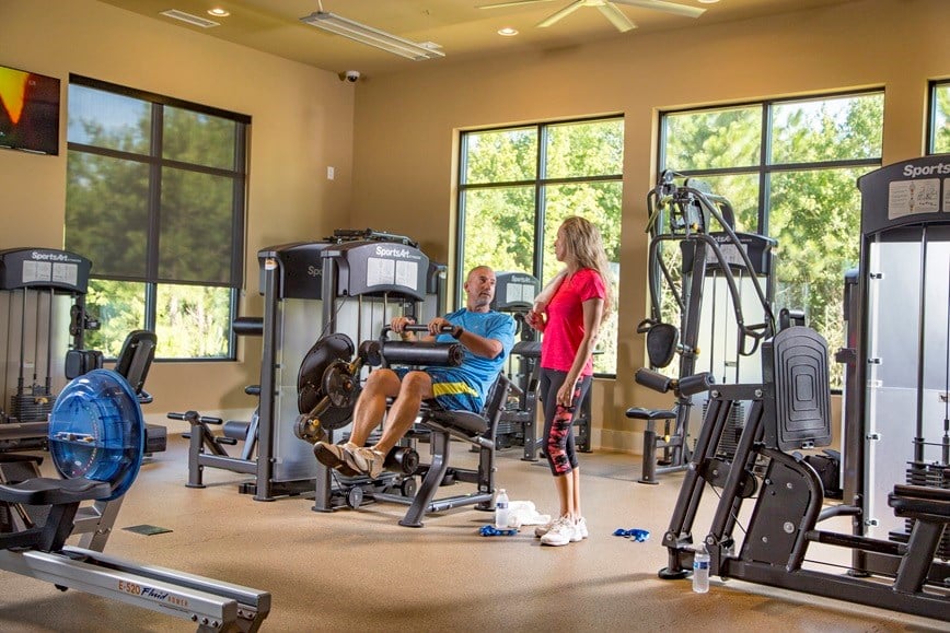 Gym with a man using a strength machine and a woman standing beside him.