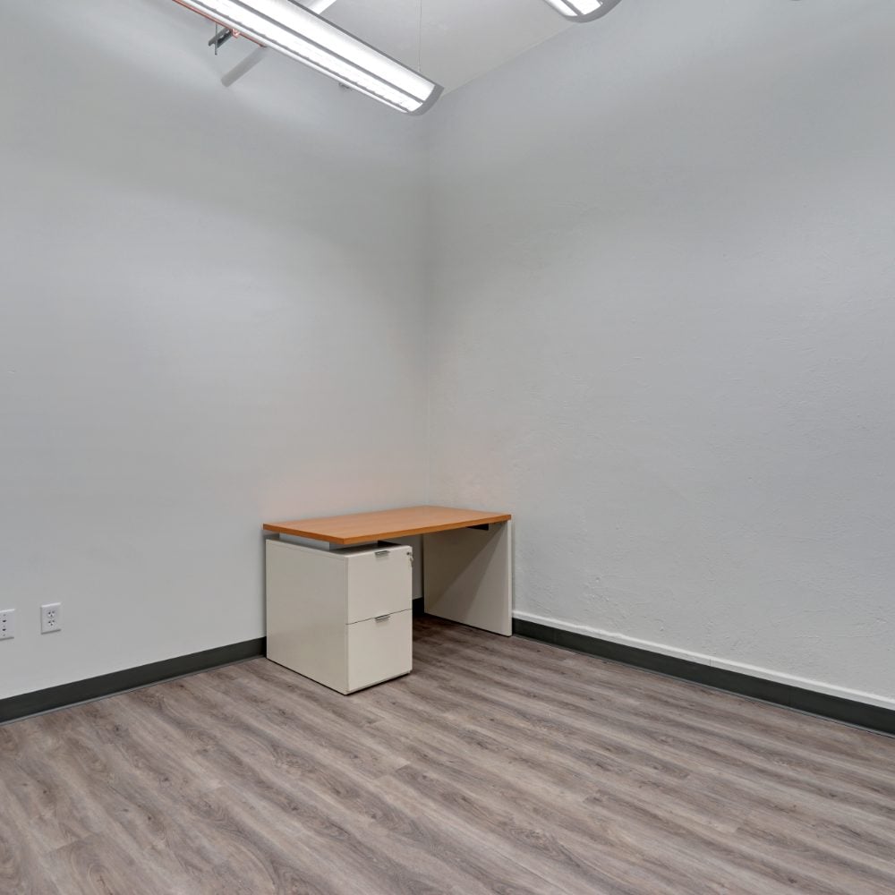 Small office with gray wood-look flooring and a desk beside a two-drawer filing cabinet.