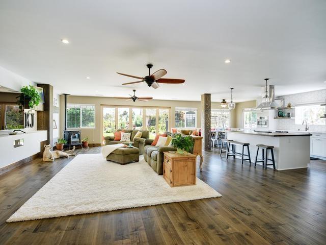 Open-plan living room and kitchen with a white island, wide windows, and a furnished seating area.