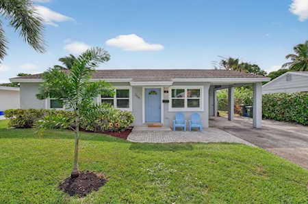 Single-story home with a small palm tree in the lawn, blue chairs by the entrance, and a covered carport.