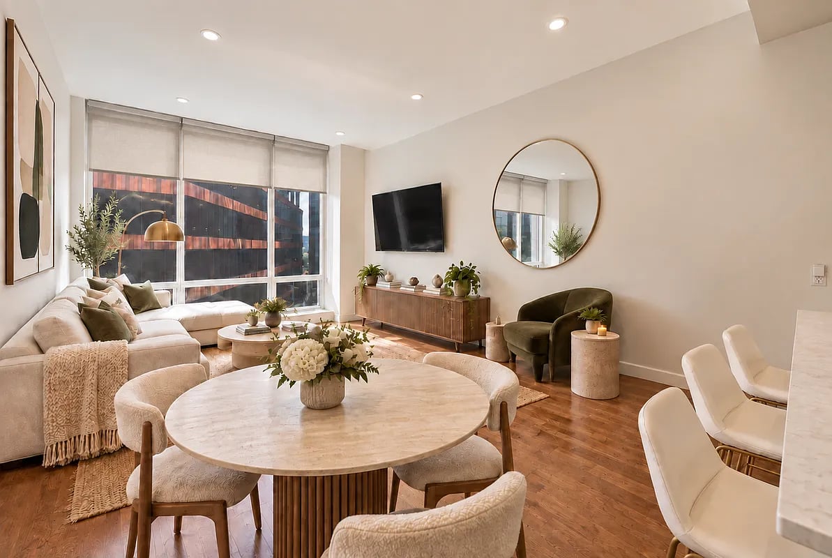 Staged living and dining room with a cream sectional, round marble table, and large windows.