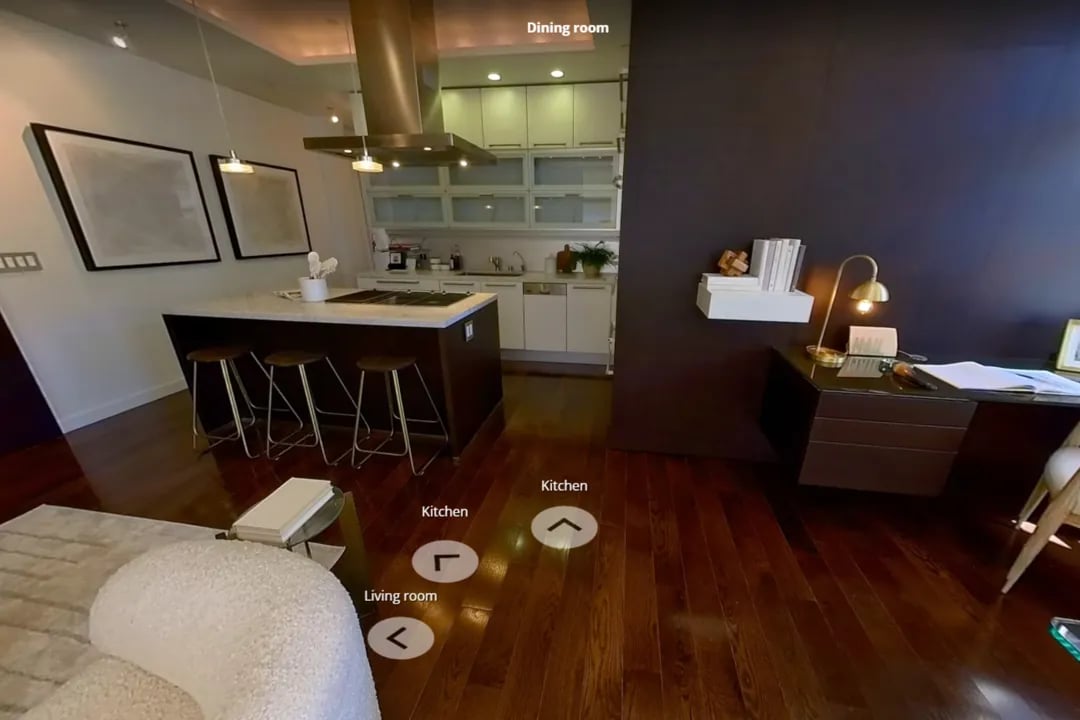 3D virtual home tour showing modern open-concept kitchen with white cabinets, island with bar stools, and navigation labels for Kitchen, Living room, and Dining room areas on dark hardwood floors.