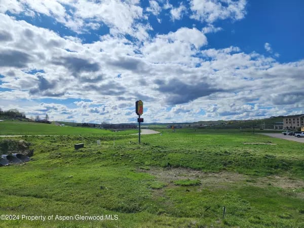 Green open field beside a road, with low hills and a cloud-filled sky.