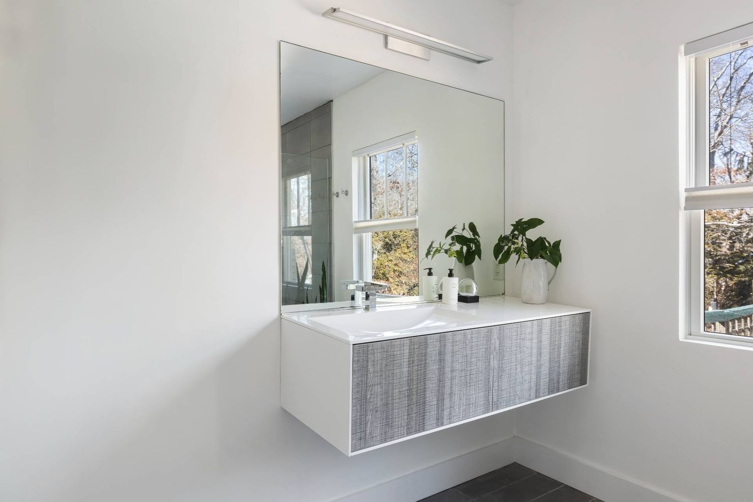 Modern bathroom with a floating gray vanity, integrated sink, and large mirror beside a window.