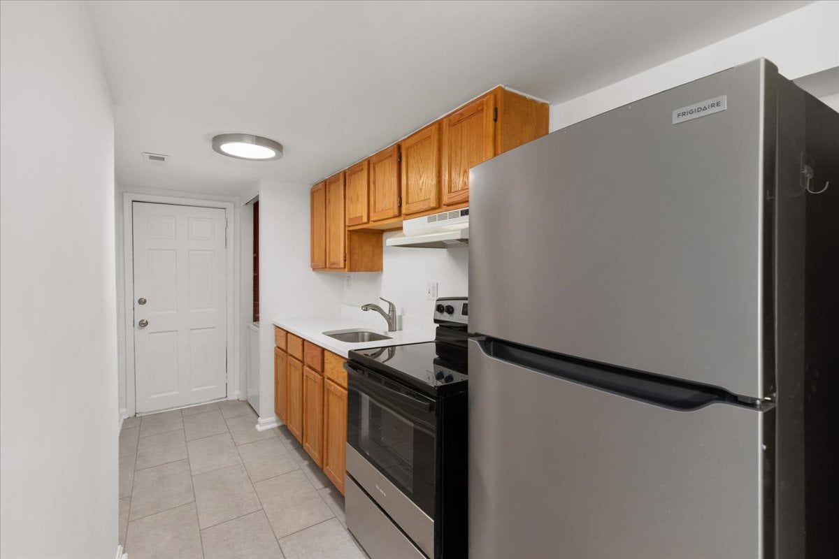 Compact kitchen with wood cabinets, stainless steel refrigerator, and black electric range.