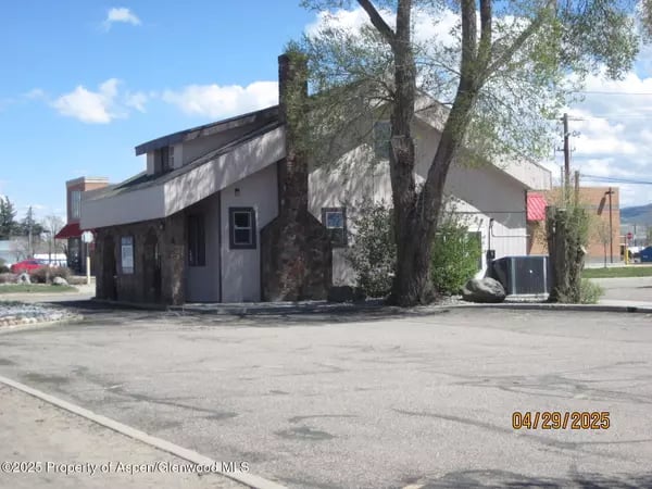 Low, angular commercial building with stone accents and a large tree beside the paved parking area.