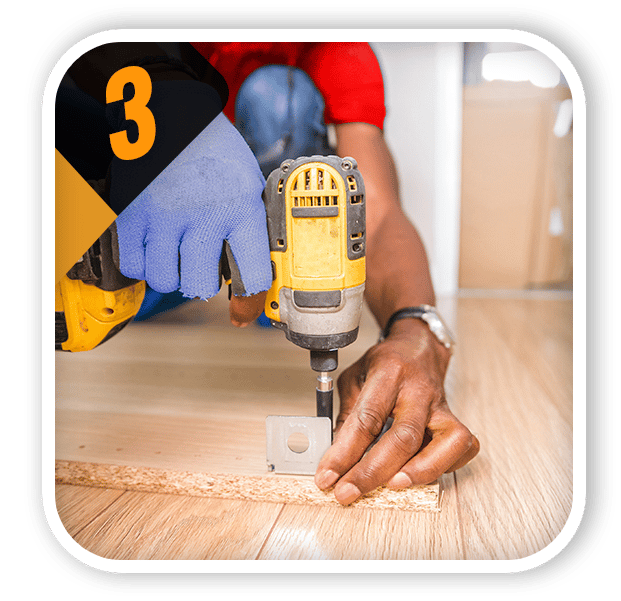 Worker uses a drill to fasten a metal bracket to wood flooring.