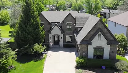 Aerial view of a two-story brick home with steep gabled roofs and a wide driveway.