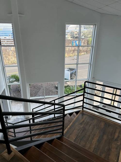 Commercial property staircase with dark wood steps, black metal railings, and tall street-facing windows.
