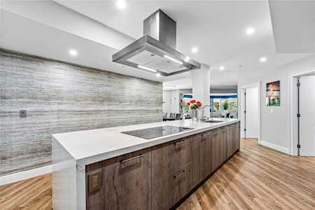Modern kitchen with a long white island, dark wood cabinets, and a gray stone backsplash.