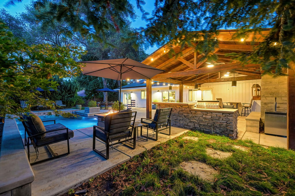 Backyard pool and covered patio with a stone-bar outdoor kitchen at dusk