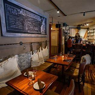 Rustic restaurant dining room with wooden tables, a cushioned bench, and a chalkboard menu.