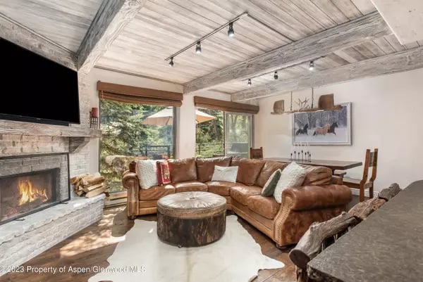 Living room with exposed timber ceiling, stone fireplace, and brown leather sectional.