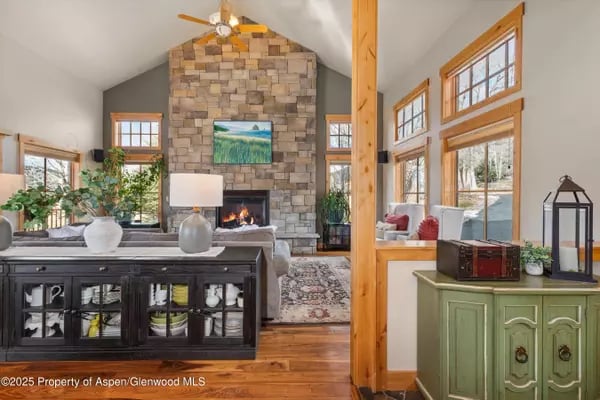 Living room with a tall stone fireplace, vaulted ceiling, and large windows.
