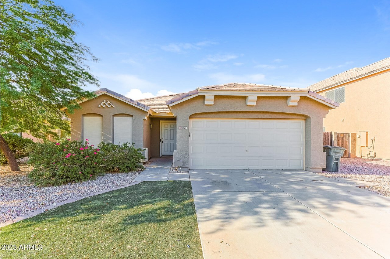 Single-story stucco home with a double garage, tiled roof, and flowering shrubs beside the driveway.