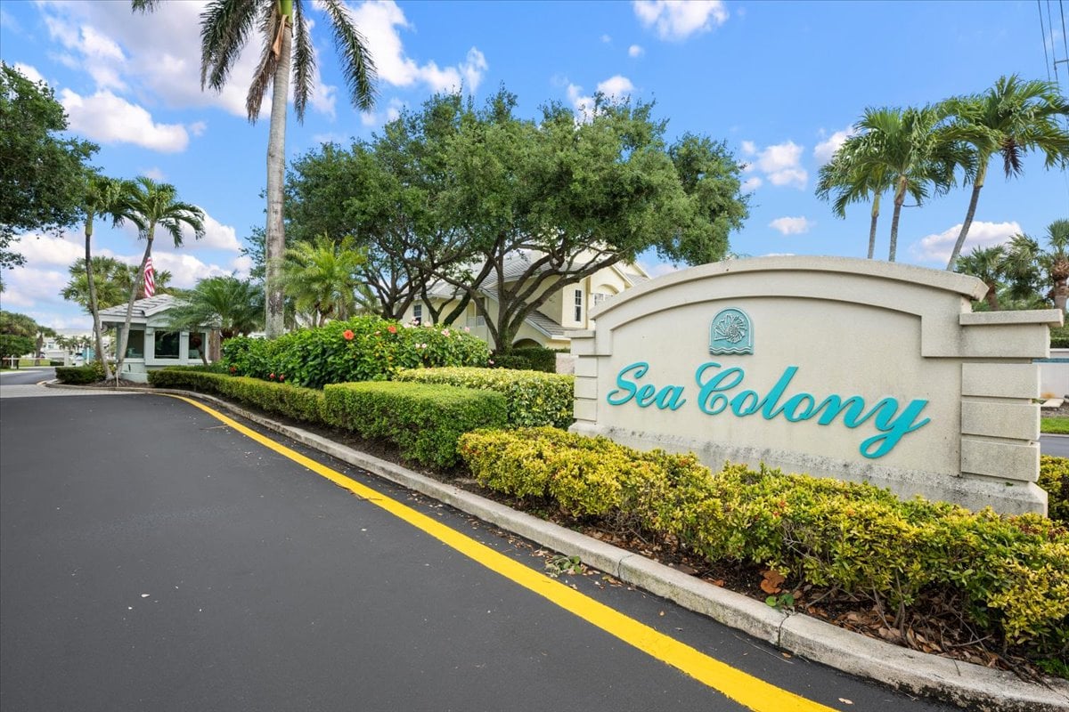 Sea Colony Condominium entrance sign beside a palm-lined driveway and landscaped hedges.