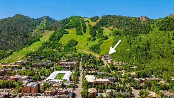 Aerial view of Aspen beneath green mountain slopes, with an arrow pointing toward buildings.