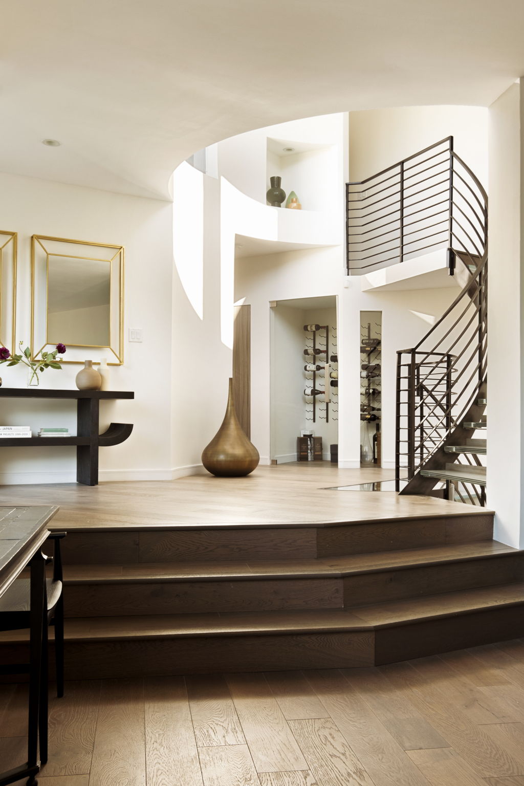 Foyer with a sweeping dark wood staircase, curved metal railing, and glass wine display.