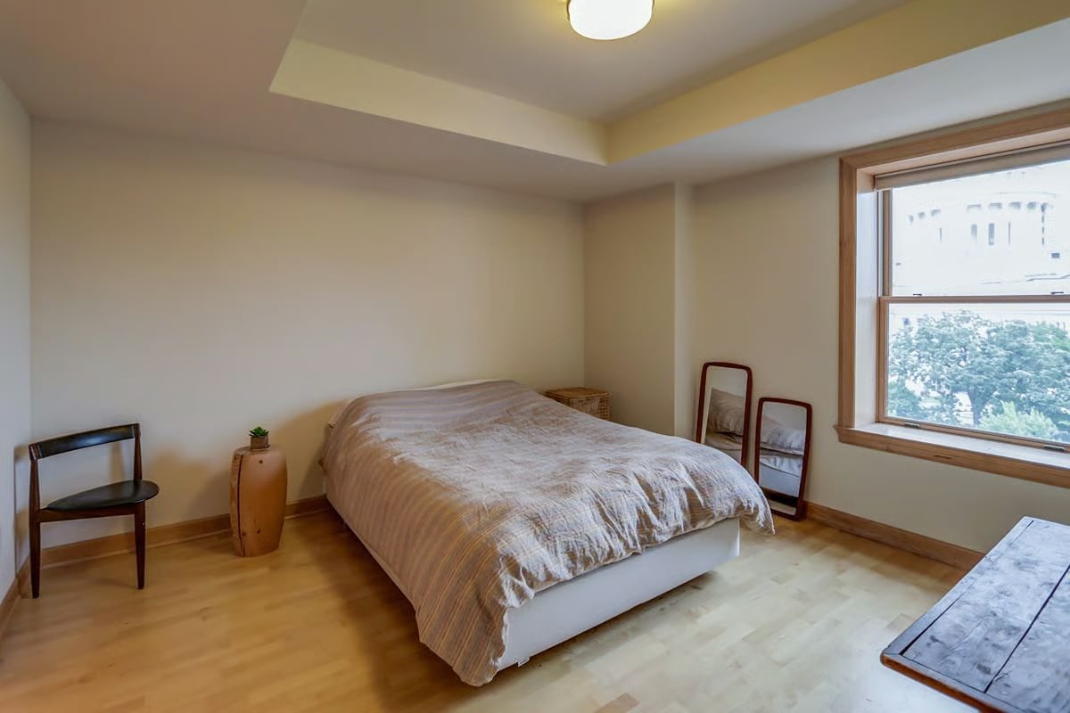 Bedroom with a low bed and large window overlooking trees and a light-colored building.