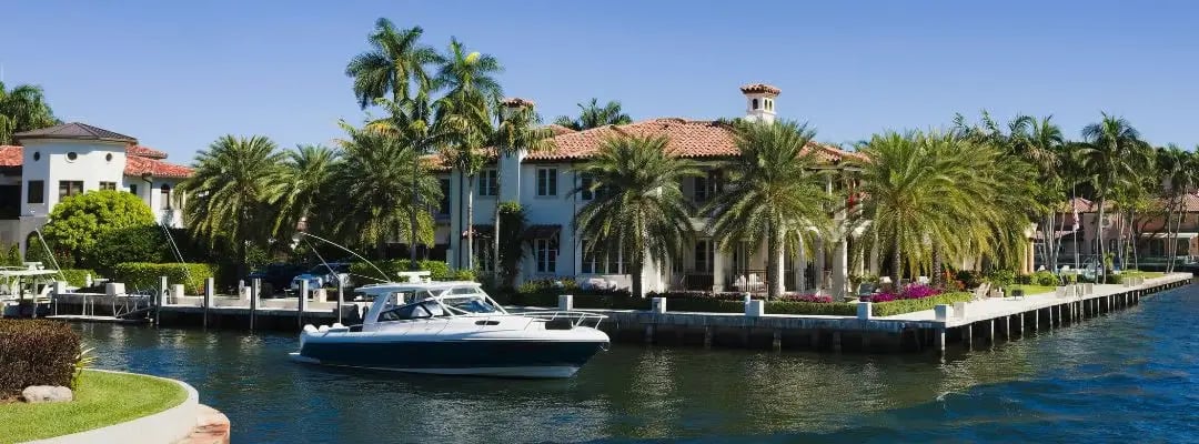Waterfront homes with palm trees line a canal beside a motorboat.