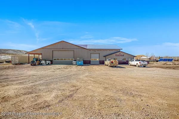 Metal-sided industrial building with garage doors and vehicles on a wide gravel lot.
